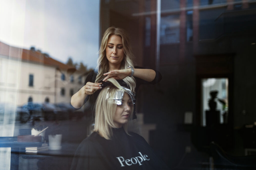 Frisör slingar en kunds hår, sett genom salongens fönster på Västergatan